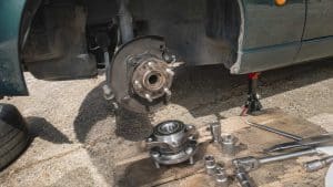 gros plan du moyeu avant démonté d'une Mazda MX-5 NB sur chandelle, roulement de roue neuf posé sur une planche avec douilles et clé à cliquet, 22 juillet 2026, format 16:9