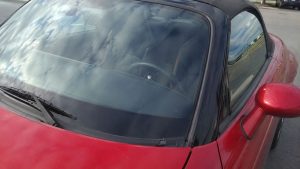 Impact de gravillon avec fissures en étoile au centre du pare-brise d'une Mazda MX-5 NB rouge