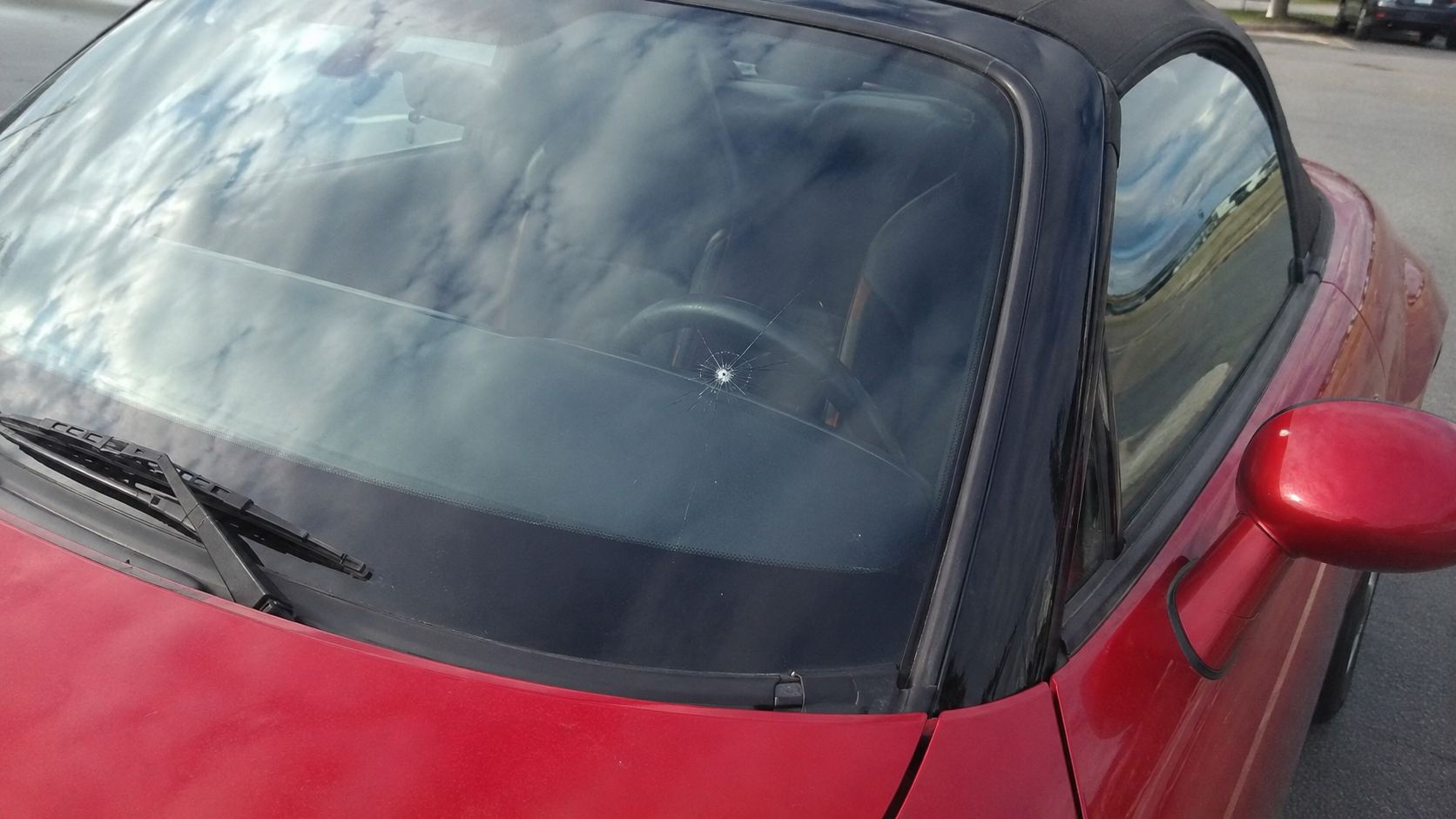 Impact de gravillon avec fissures en étoile au centre du pare-brise d'une Mazda MX-5 NB rouge