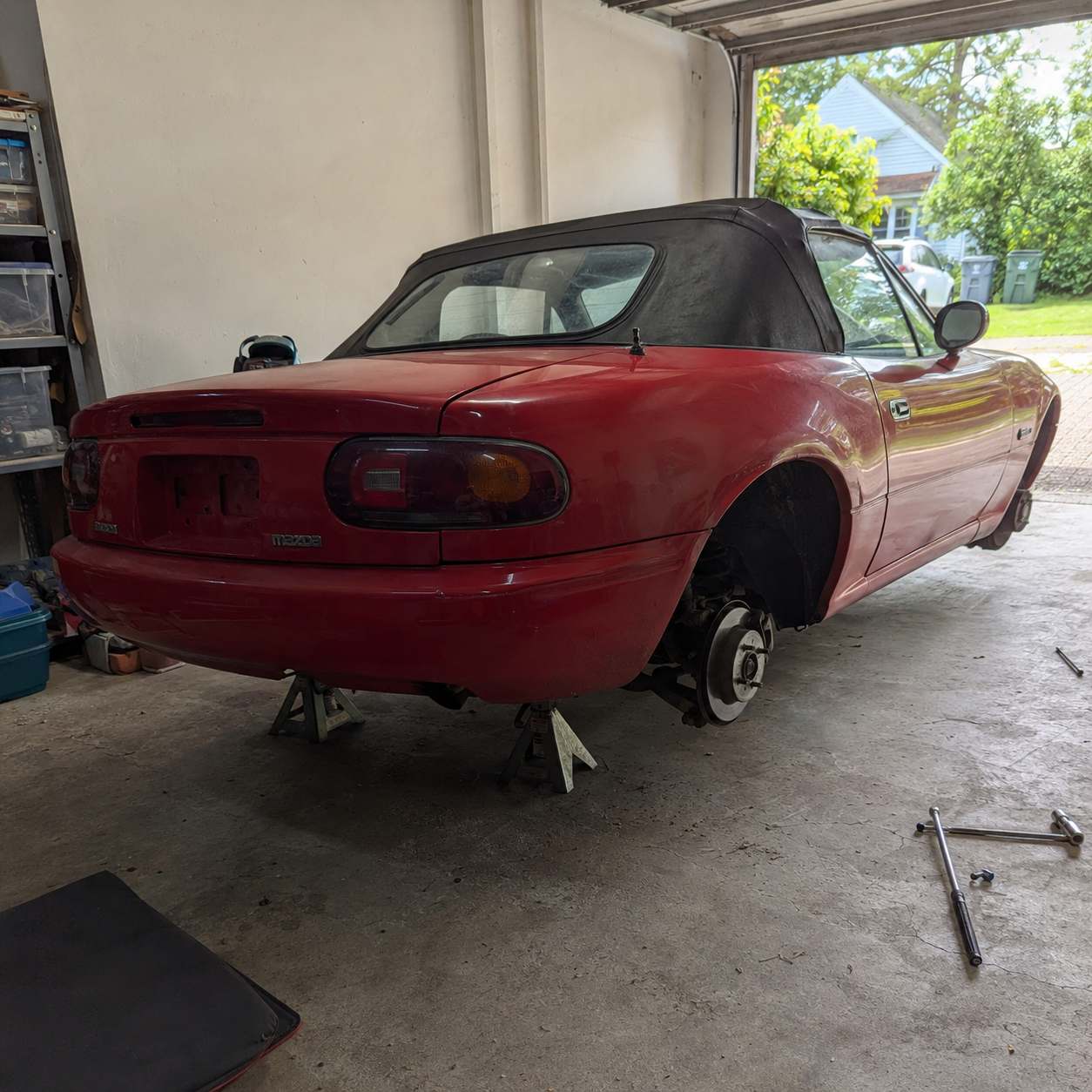 Mazda MX-5 NA rouge sur chandelles, roue arrière déposée laissant voir moyeu et disque de frein