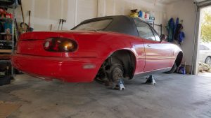 Mazda MX-5 NA rouge sur chandelles dans un garage, roues déposées et freins à nu