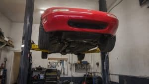 Mazda MX-5 NA rouge vue de dessous sur un pont élévateur deux colonnes en atelier