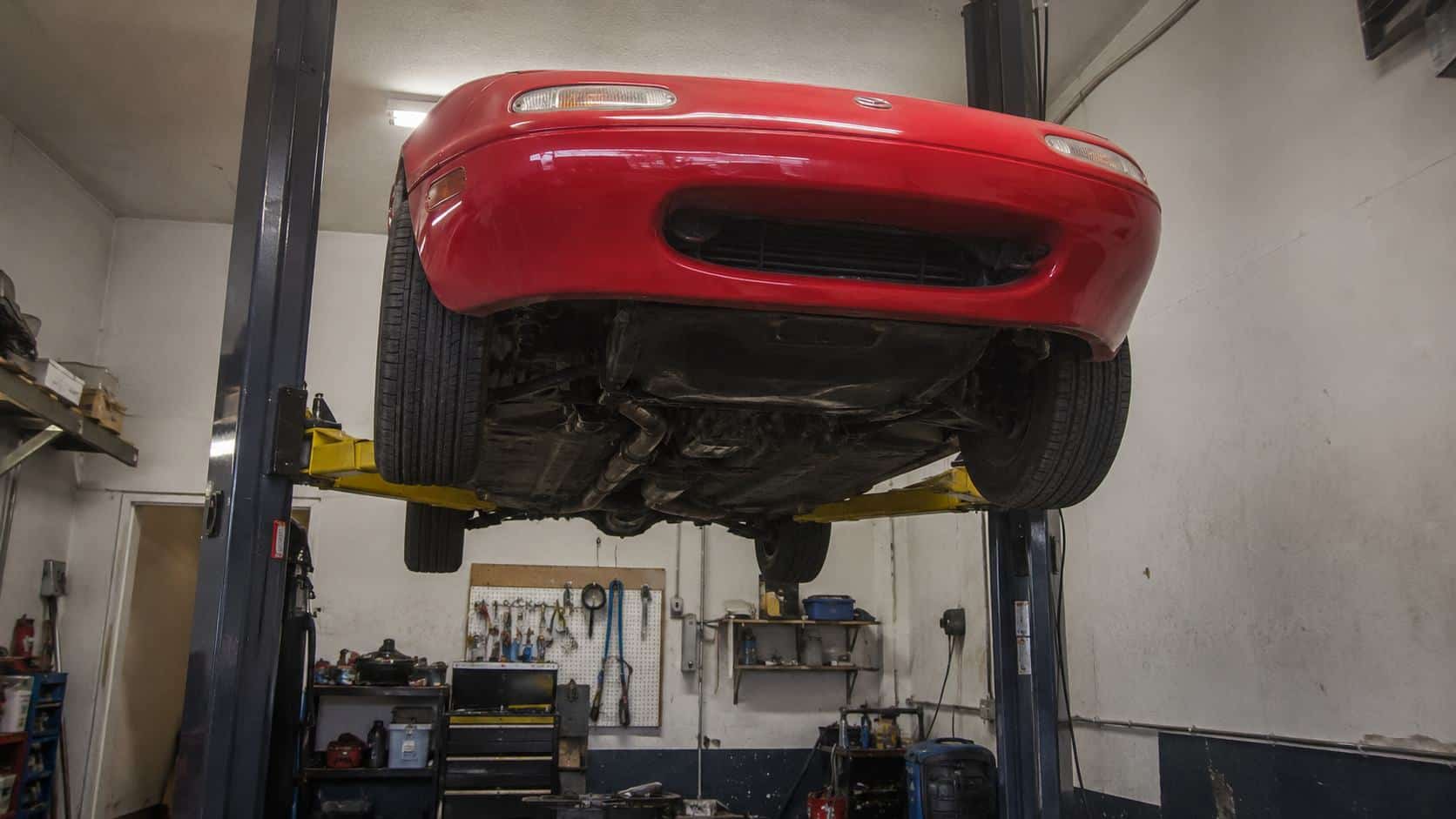 Mazda MX-5 NA rouge vue de dessous sur un pont élévateur deux colonnes, train avant dégagé