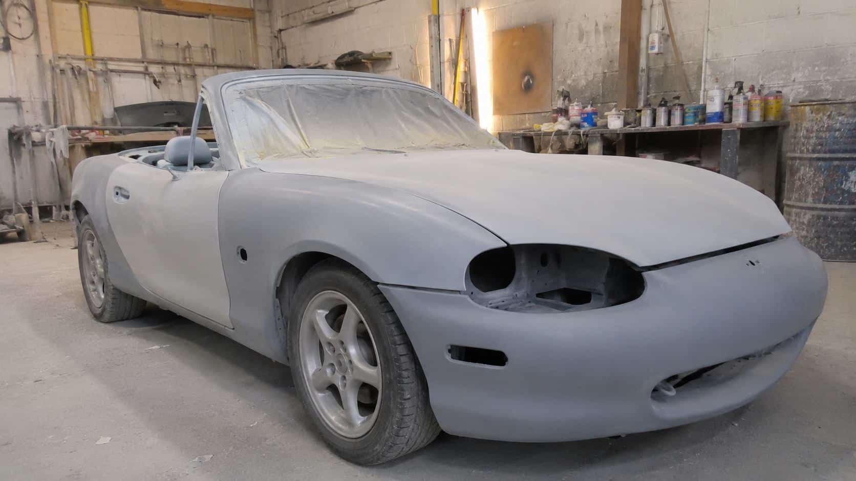 Mazda MX-5 NB recouverte d'apprêt gris mat avec vitrage masqué dans un atelier de peinture