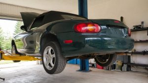 Mazda MX-5 NB verte levée sur un pont élévateur deux colonnes, vue arrière en atelier