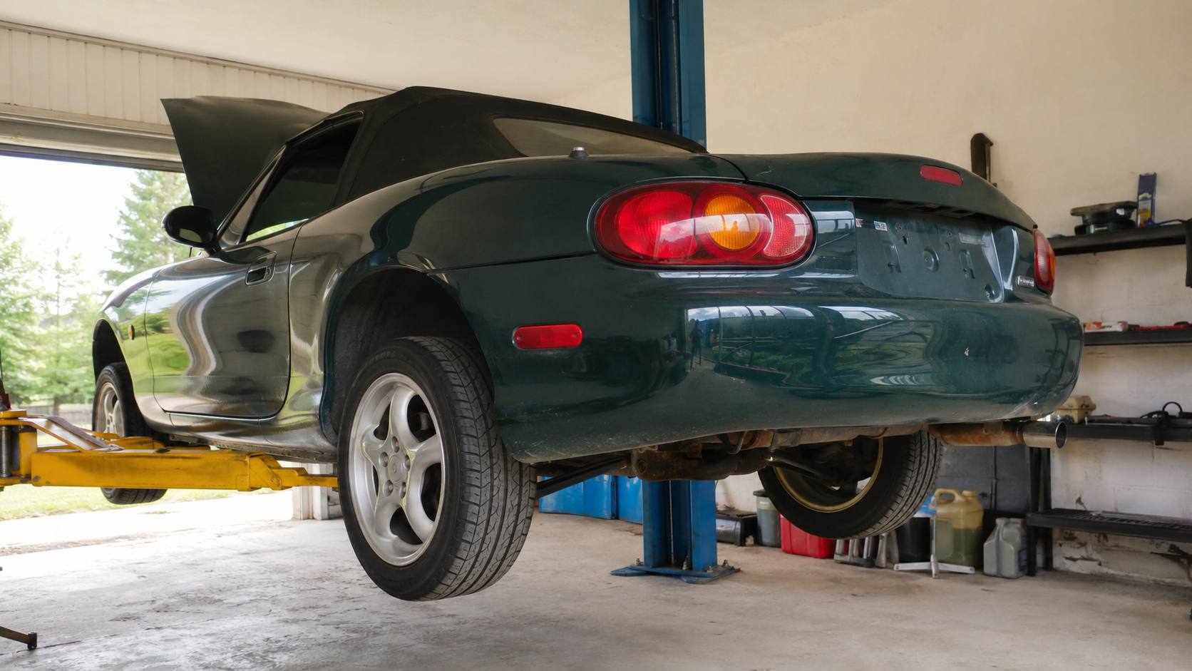 Mazda MX-5 NB verte levee sur un pont elevateur deux colonnes dans un atelier