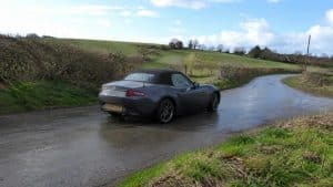 Mazda MX-5 ND gris anthracite sur une petite route de campagne mouillée bordée de haies