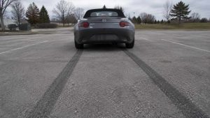 Mazda MX-5 ND grise vue de l'arrière sur un parking désert avec deux longues traces de gomme au sol