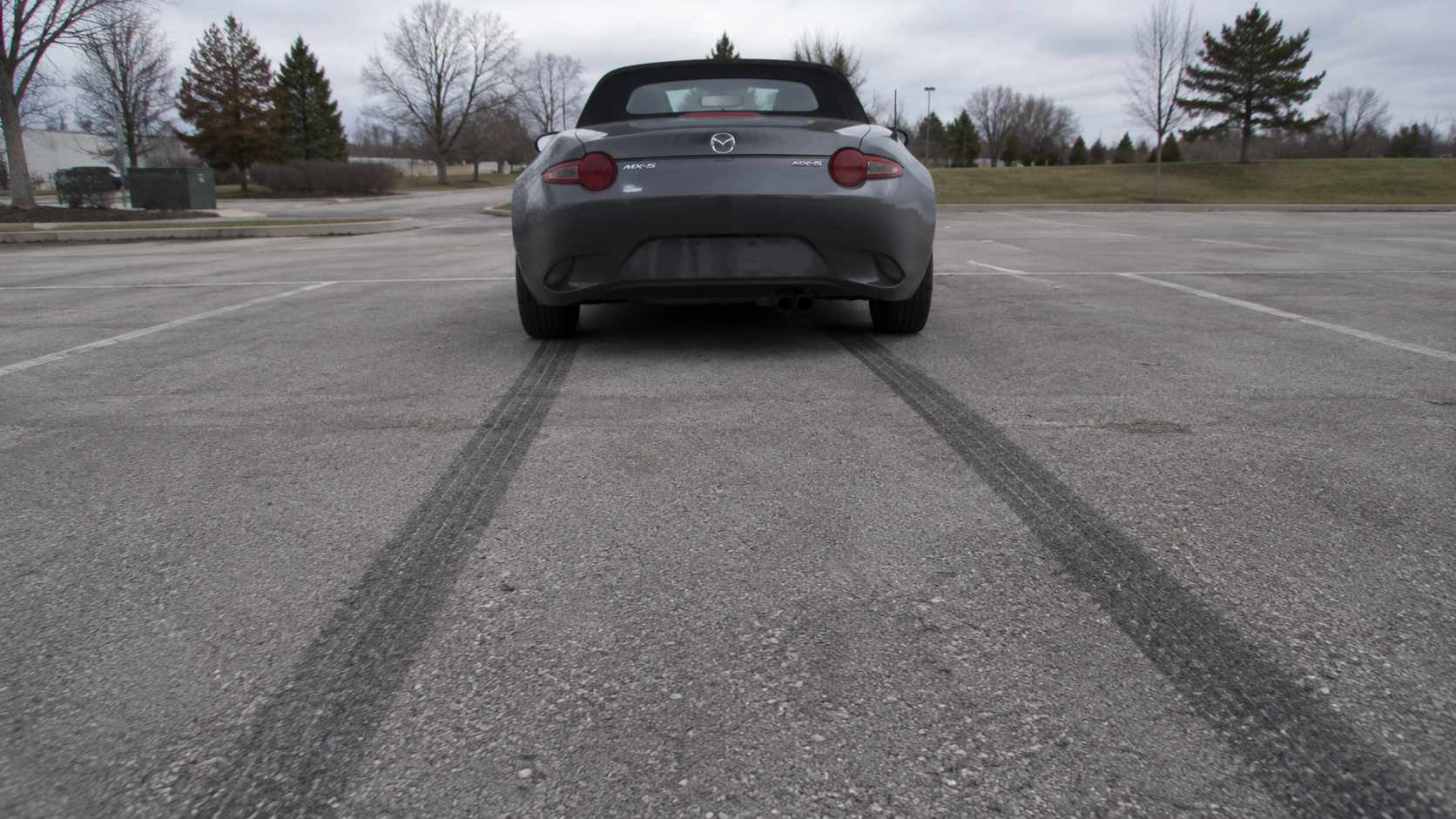 Mazda MX-5 ND grise vue de l'arrière avec deux traces de gomme au sol sur un parking