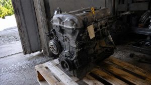 Moteur quatre cylindres de Mazda MX-5 déposé sur une palette en bois dans un atelier, jauge jaune visible