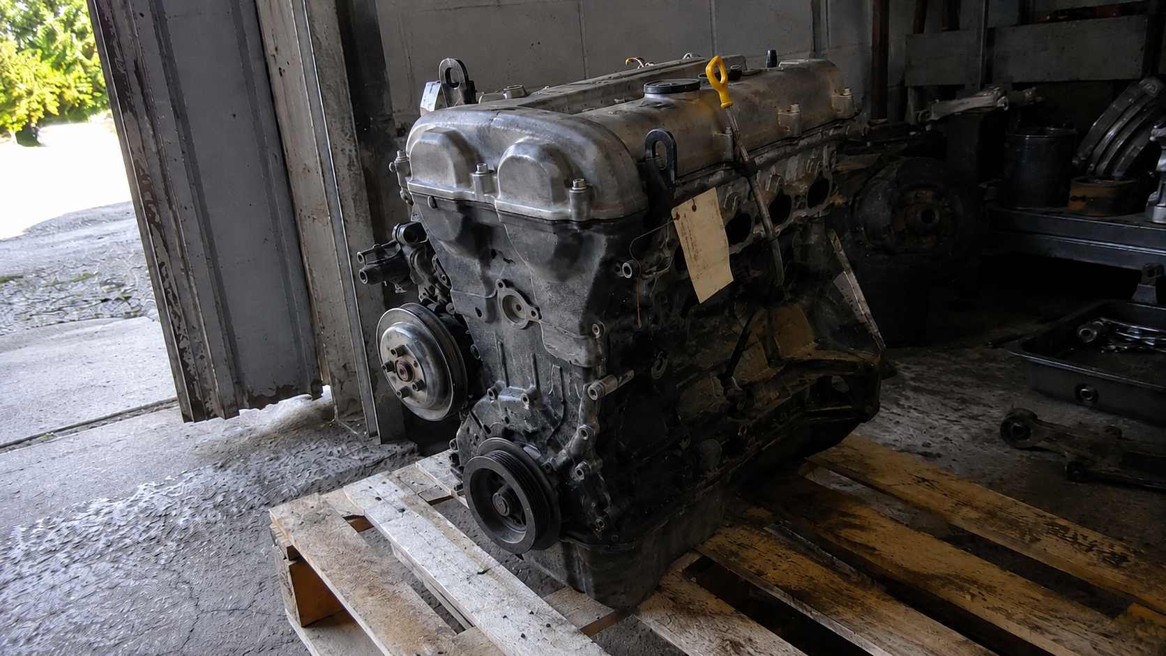 Moteur quatre cylindres de Mazda MX-5 déposé sur une palette en bois dans un atelier, jauge jaune visible