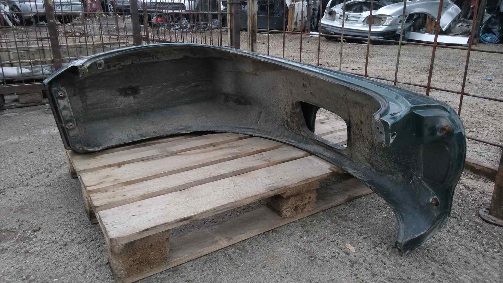 Pare-chocs arrière vert de Mazda MX-5 NB d'occasion posé sur une palette devant les grilles d'une casse auto