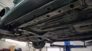 Seuil gauche et plancher du soubassement d'une Mazda MX-5 verte vus en contre-plongée sur pont élévateur