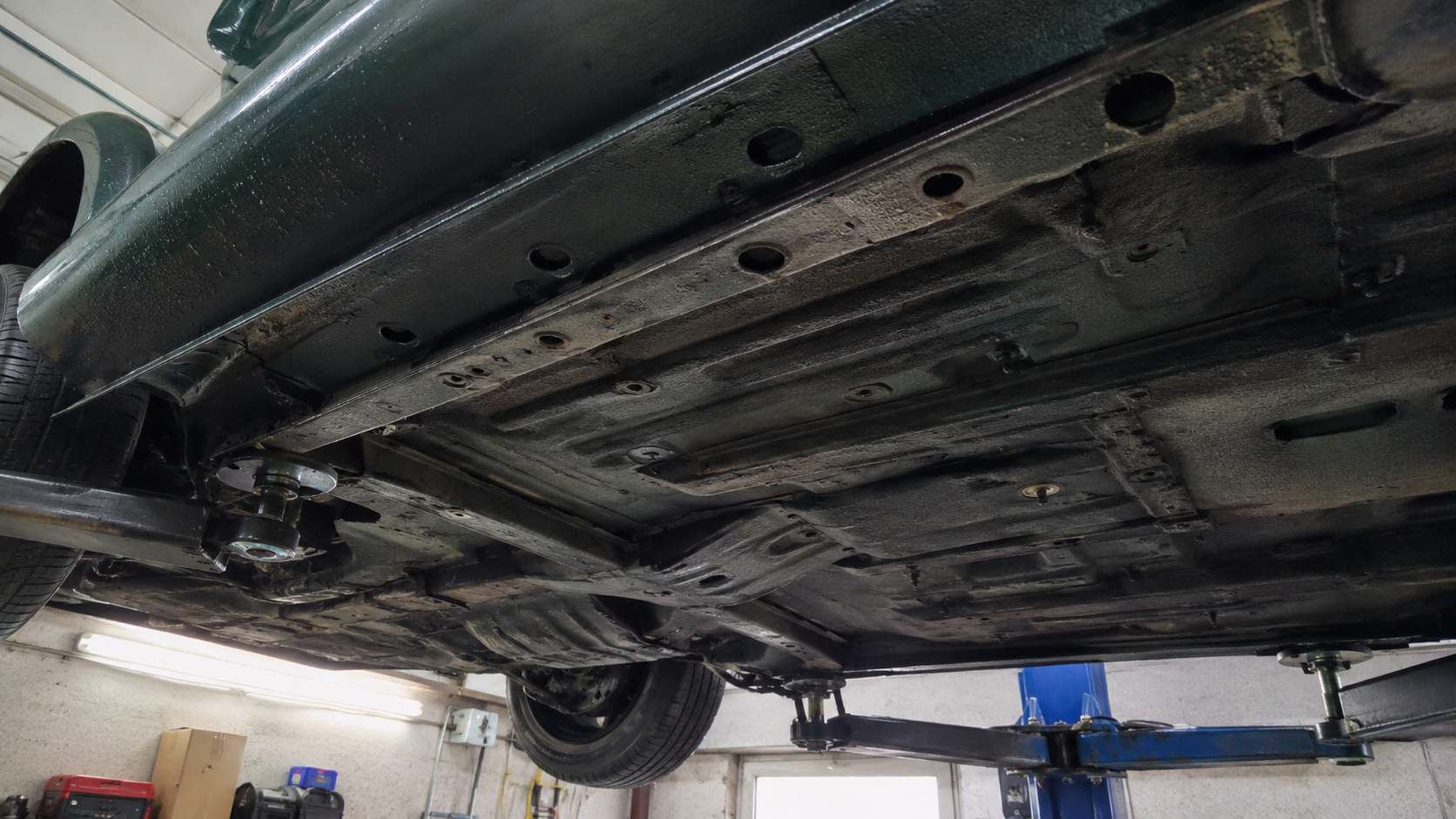 Seuil gauche et plancher du soubassement d'une Mazda MX-5 verte vus en contre-plongée sur pont élévateur