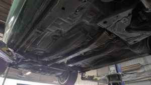 Soubassement arrière d'une Mazda MX-5 verte avec tunnel et câbles de frein à main, vue sur pont en atelier