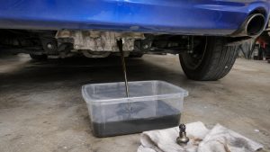 Huile usagée s'écoulant du différentiel d'une Mazda MX-5 bleue dans un bac, bouchon magnétique posé sur un chiffon