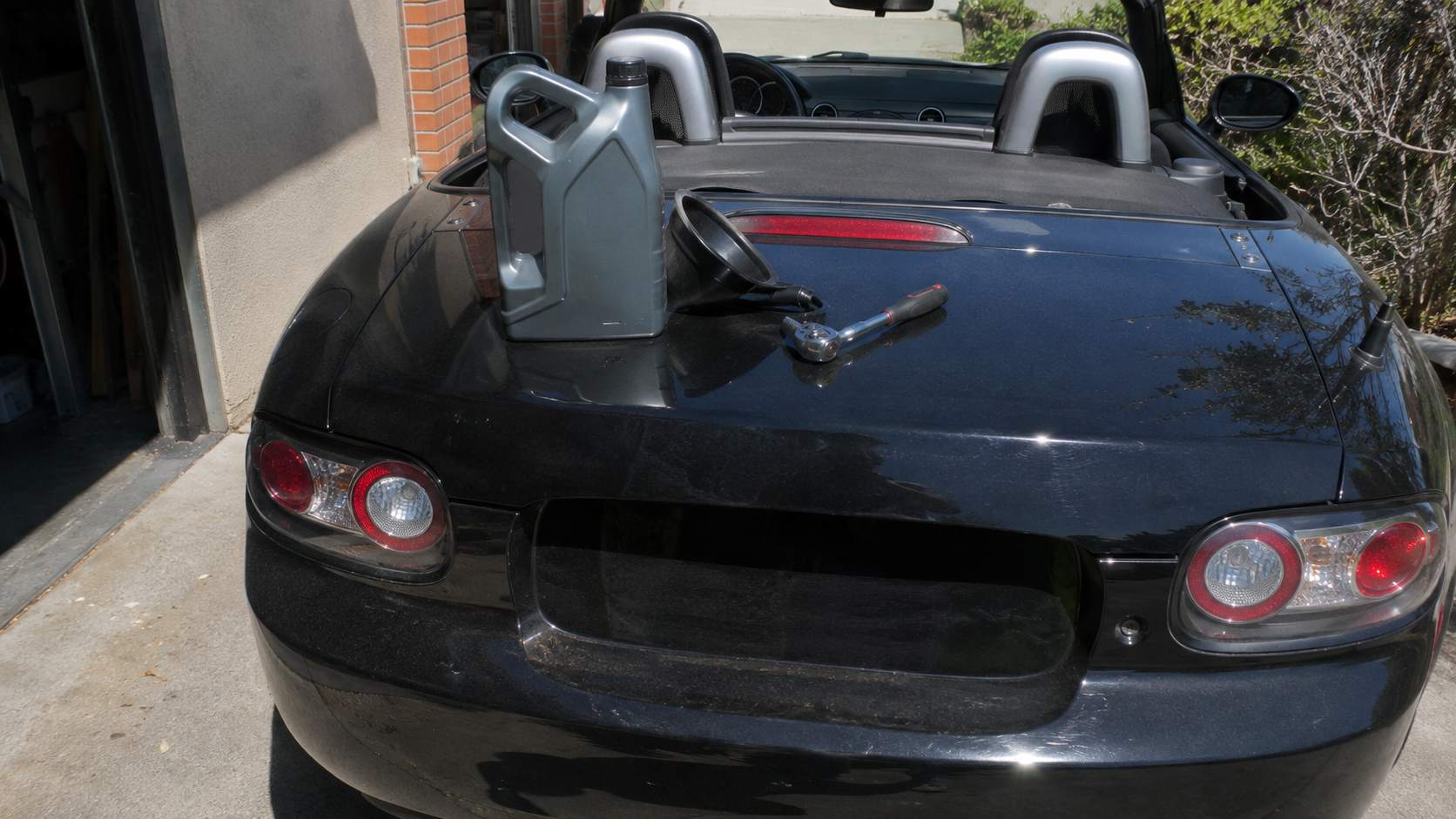 Remplissage d'huile moteur sur une Mazda MX-5 NC noire avec bidon et entonnoir